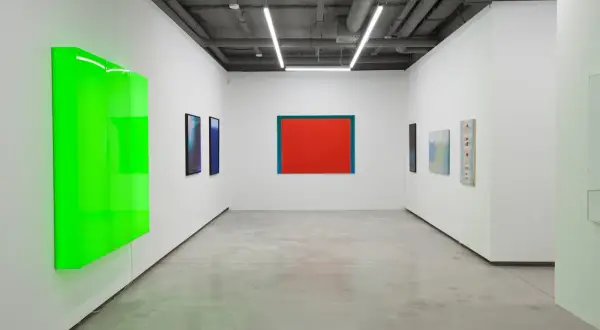 Galeria sztuki z neonowo-zieloną instalacją i obrazami, w tym dziełem Stefana Gierowskiego.