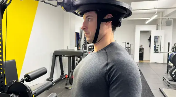 Man performing neck curls with a weighted harness in a gym.