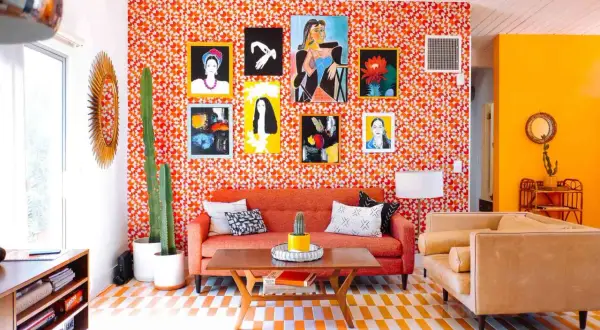 Vibrant living room with a bold 70s aesthetic. Orange patterned wallpaper, a cactus, and colorful art create a retro vibe.