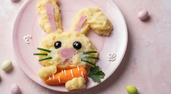 Un adorable lapin en purée de pommes de terre, parfait pour une entrée de Pâques sans œufs. Il tient une carotte et des œufs de Pâques sont autour.