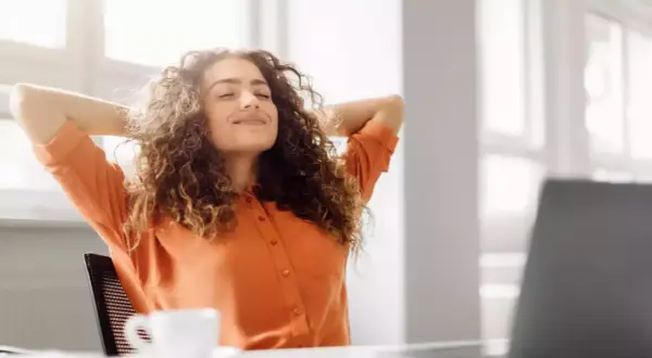Femme souriante, mains derrière la tête, profitant d'une pause. Son retour congé maternité obligation employeur semble bien se passer.