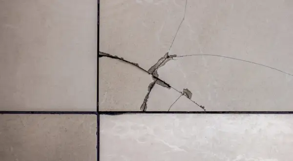 Gros plan sur un carrelage beige fissuré, montrant les étapes pour comment reparer un eclat de carrelage.