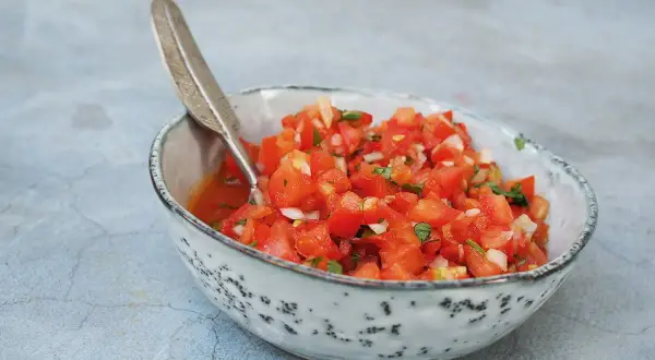 En skål med färsk pico de gallo, perfekt för ditt salsa recept. Tomater, lök och örter blandas i en rustik skål med en dekorativ sked.