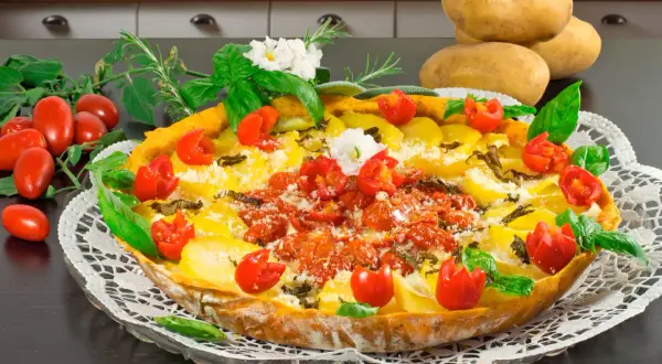 Herzhafte torta salata mit Kartoffeln, Tomaten und Kräutern, garniert mit frischem Basilikum und kleinen weißen Blüten.
