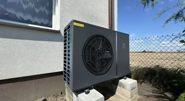 Nowoczesna pompa ciepła Geo Power, która obniża koszt ogrzewania domu. Urządzenie stoi na betonowych bloczkach przy ścianie budynku.