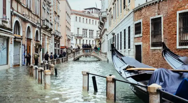 Venecia cuando se inunda: góndolas esperan en canales crecidos, peatones cruzan un puente sobre el agua que llega a las puertas de las tiendas.