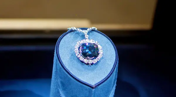 Niebieski diament Hope, otoczony mniejszymi kamieniami, lśni na aksamitnym postumencie.