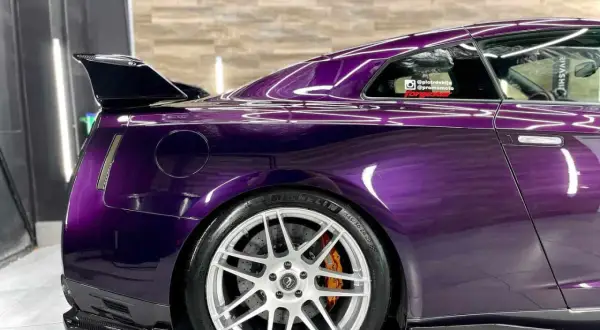 Sportowy Nissan GT-R w odcieniu **midnight purple**, z karbonowym spoilerem i felgami.