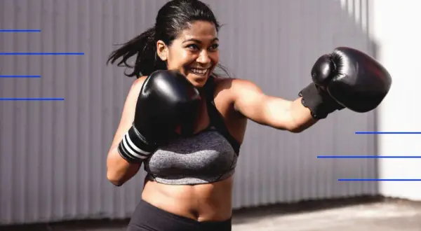 A woman with a big smile is throwing a punch with her boxing gloves on, ready to take on any challenge.