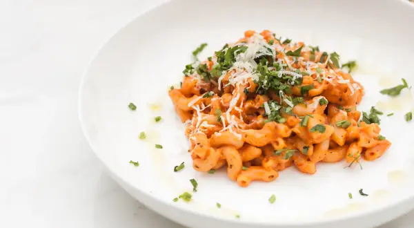 Penne alla vodka z posiekaną natką pietruszki i startym parmezanem na białym talerzu.