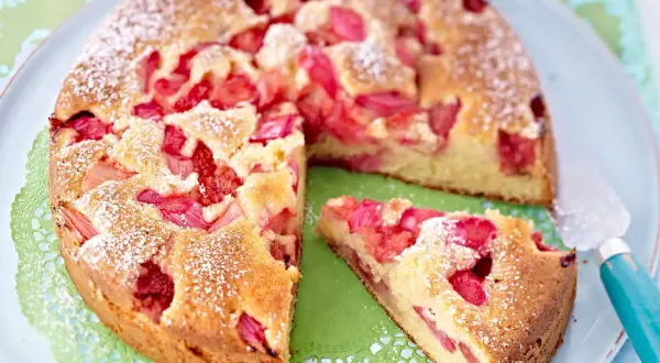 Ein saftiger Erdbeer Rhabarber Kuchen, bestäubt mit Puderzucker, wartet auf seinen Genuss. Ein Stück ist bereits herausgeschnitten.