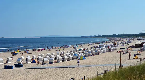 Plaża nad Bałtykiem z rzędami koszy plażowych, ludźmi i morzem w tle.