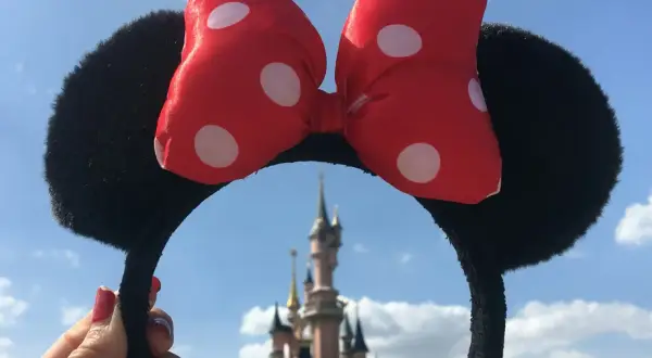 Opaska z uszami Myszki Miki i czerwoną kokardką w kropki, na tle zamku. Czyżby to początek przygody z księżniczki Disneya imiona?