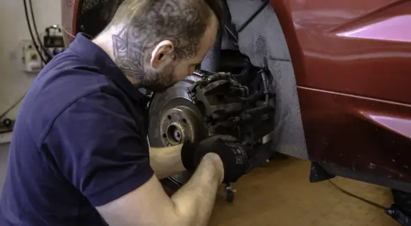 Mechanik w rękawiczkach naprawia hamulce w czerwonym Volvo. Dbałość o szczegóły zapewnia długą gwarancję.