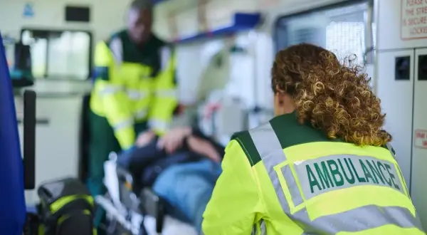 Personale sanitario assiste paziente su barella in ambulanza, garantendo il trasporto sicuro secondo la legge 104.