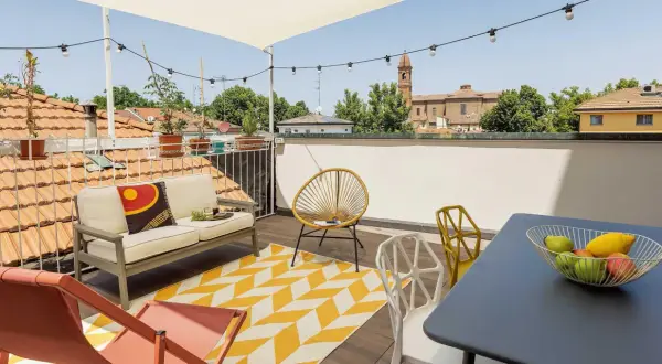 Un accogliente terrazzo sul tetto con divano, sedie colorate e un tappeto geometrico. Ideale per godersi il panorama urbano e rilassarsi.