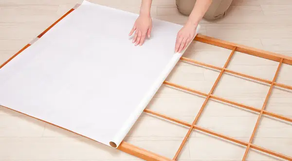 Mains déroulant du papier pour fabriquer une cloison japonaise sur un cadre en bois.