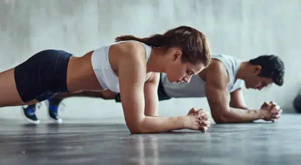 Un couple s'entraîne ensemble, concentré sur leur gainage abdos dans une salle de sport.