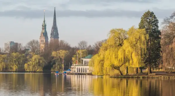 Ein idyllischer Blick auf den Alstersee in Hamburg. Sehens. Ein Bootshaus und die Türme der Stadt spiegeln sich im Wasser.