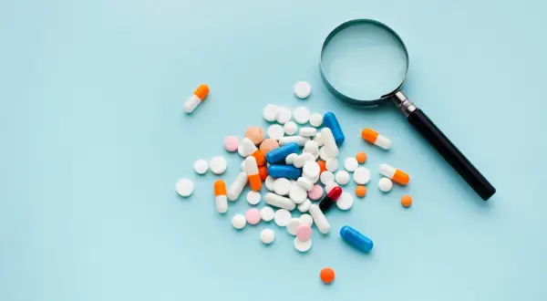En hög med olika mediciner, kapslar och tabletter, undersöks med ett förstoringsglas.