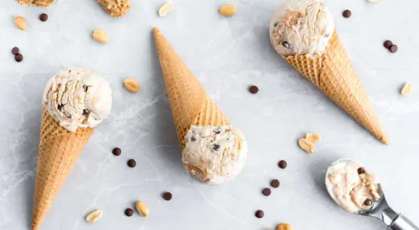 Drei Eiswaffeln mit cremigem Peanut Butter Cup Eis, umgeben von Erdnüssen und Schokostückchen.