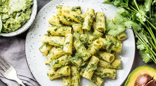 Rigatoni-Nudeln mit cremigem Avocado-Pesto, garniert mit frischem Koriander und Basilikum.