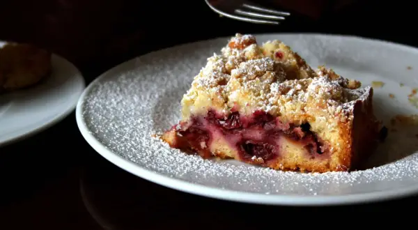Ein Stück von Omas Kirschkuchen mit Streuseln, bestäubt mit Puderzucker, wartet auf seine Gabel.
