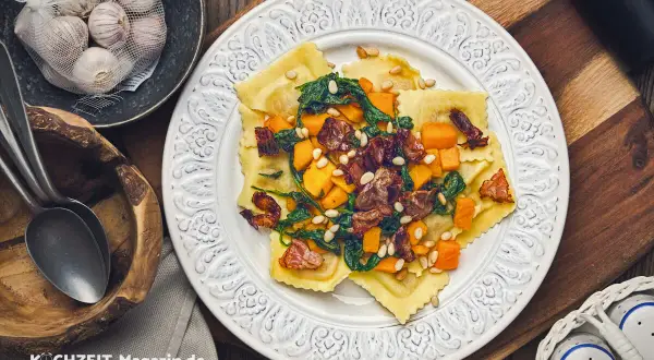 Ravioli mit Kürbis, Spinat und Pinienkernen – ein köstliches ravioli rezept. Daneben Knoblauch und Löffel.
