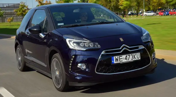 Granatowy Citroen DS3 w ruchu ulicznym. Kierowca w okularach przeciwsłonecznych. Wiele pozytywnych citroen ds3 opinie potwierdza jego styl.