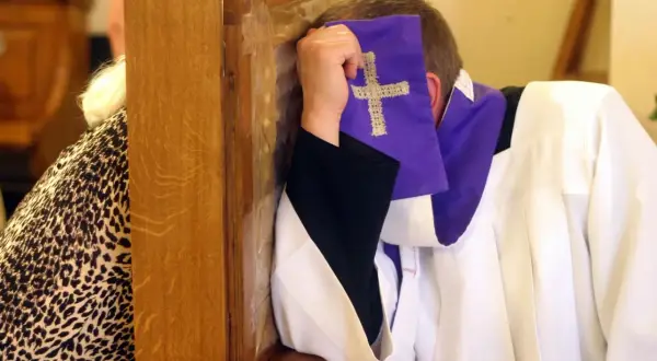 Spowiedź w konfesjonale. Czy nie pójście do kościoła w niedzielę to grzech ciężki? Duchowny w białej albie i fioletowej stulejce z krzyżem.