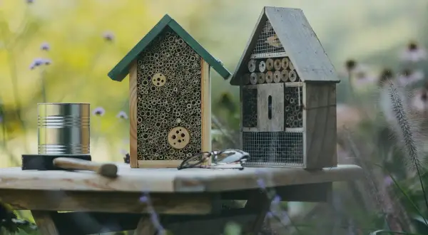 Zwei selbstgebaute Insektenhotels stehen auf einem Tisch im Garten. Ein Insektenhotel bauen ist eine tolle Idee für jeden Naturliebhaber.