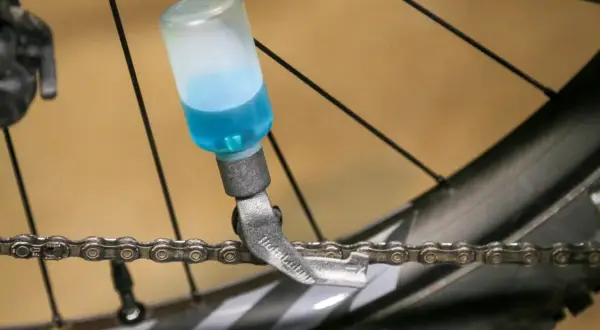 Urządzenie do smarowania łańcucha roweru z niebieskim płynem.
