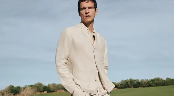 Mann in beigem Sakko und kariertem Hemd, lässig mit den Händen in den Hosentaschen. Perfekt, um ein beiges Sakko zu kombinieren für einen stilvollen Look.