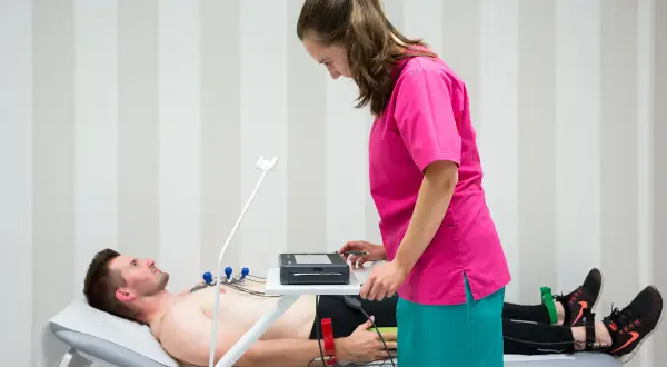 Pacjent leży na kozetce, pielęgniarka przygotowuje aparat do EKG. Badanie EKG trwa zazwyczaj kilka minut.