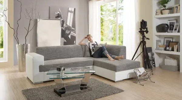 Ein modernes Wohnzimmer mit einer Frau auf dem Sofa, die liest. Der Glastisch davor ist nicht sehr hoch, perfekt für Snacks.