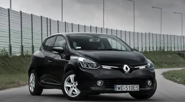 Czarny Renault Clio 4 z 2013 roku na drodze, z barierą dźwiękochłonną w tle.