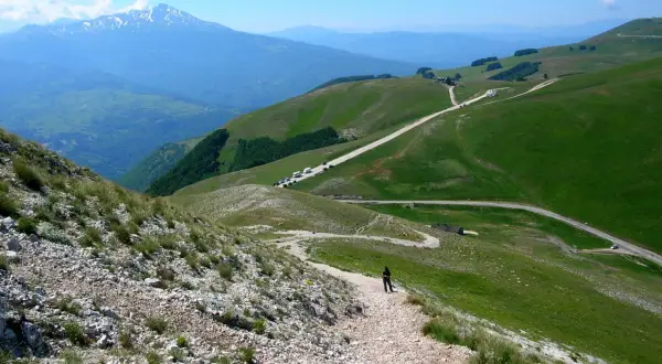 Sentiero roccioso verso la Forca di Presta, con montagne verdi e un cielo azzurro.