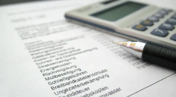 Rechnung mit Stift und Taschenrechner. Liste von Betriebskosten wie Heizung, Grundsteuer und Müllbeseitigung. Ein Widerspruch in der Betriebskostenabrechnung ist möglich.