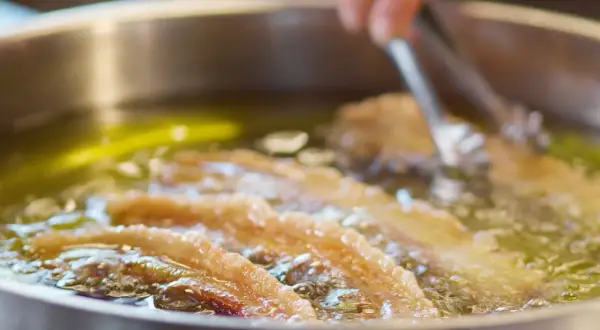 Almitas de Soria dorándose en aceite caliente. Unas pinzas metálicas manipulan la fritura.