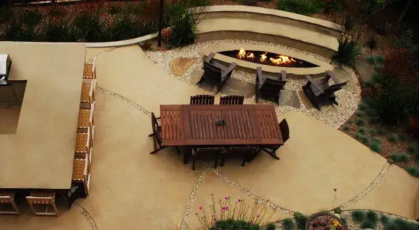 Un elegante giardino con un'area salotto attorno a un focolare, il tutto su un raffinato rivestimento in cemento per esterni.