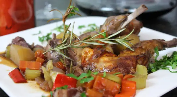 Zart gebratener kaninchen braten in der pfanne, serviert mit Kartoffeln, Karotten, Sellerie und Paprika, garniert mit Rosmarin.