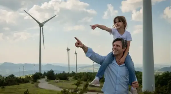 Ojciec z córką na ramionach wskazują na farmę wiatrową. Pozytywne polenergia opinie.