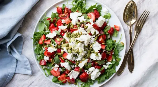 En fräsch sallad med jordgubbar, fetaost och pumpafrön på en vit tallrik.