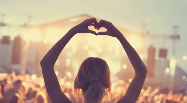 Ragazza fa un cuore con le mani a un concerto, immersa nell'atmosfera delle canzoni romantiche inglesi.