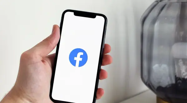 Dłoń trzyma smartfon z logo Facebooka. Dowiedz się, jak wstawić ogłoszenie na FB, by dotrzeć do szerokiego grona odbiorców.