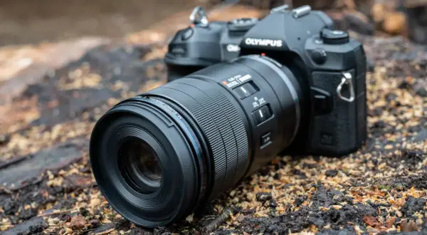 An Olympus camera with a Micro Four Thirds pancake lens rests on a bed of wood chips and dark soil, ready for an outdoor adventure.