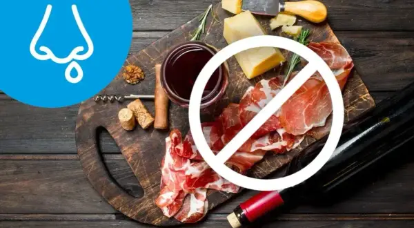 Na desce ser, wędliny i wino, przekreślone symbolem zakazu. Obok symbol nosa z kropelką, sugerujący dietę antyhistaminową.