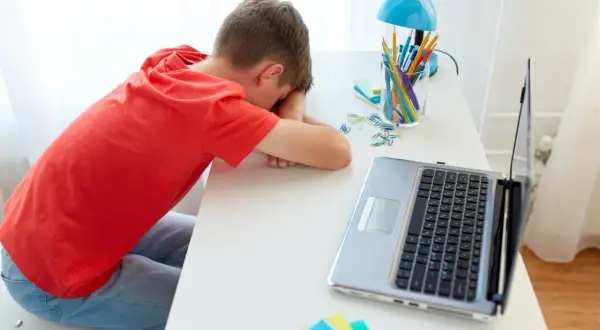 Chłopiec śpi na biurku obok laptopa i przyborów szkolnych.