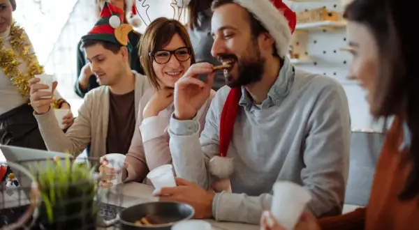 Fröhliche Menschen feiern Weihnachten. Sie tragen Weihnachtsmützen und trinken. Ist Heiligabend ein Feiertag? Ja, und sie genießen ihn!