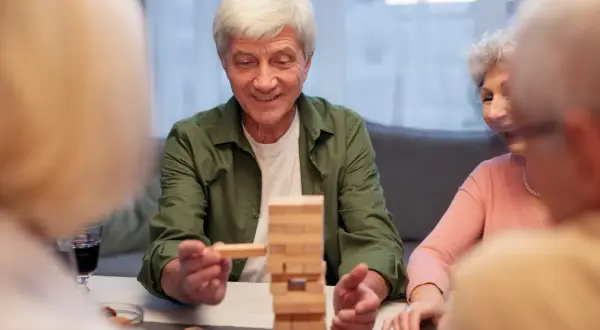 Un homme âgé sourit en retirant un bloc d'une tour Jenga. Un jeu stimulant pour la mémoire, utile dans le cadre d'un jeu Alzheimer.